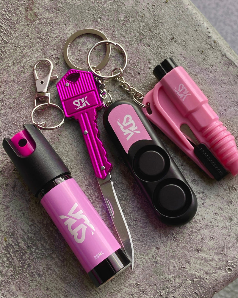 Pink self defense tool laid out. pepper spray, key knife, safety alarm, car escape tool